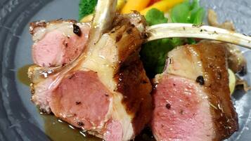 A dish of lamb chops with a sauce, accompanied by vegetables and a decorative element.