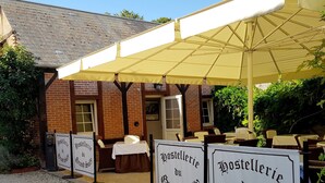 A restaurant with outdoor seating under a large canopy, surrounded by gravel and a brick building. - Hostellerie du Grand Sully (Sully-sur-Loire)