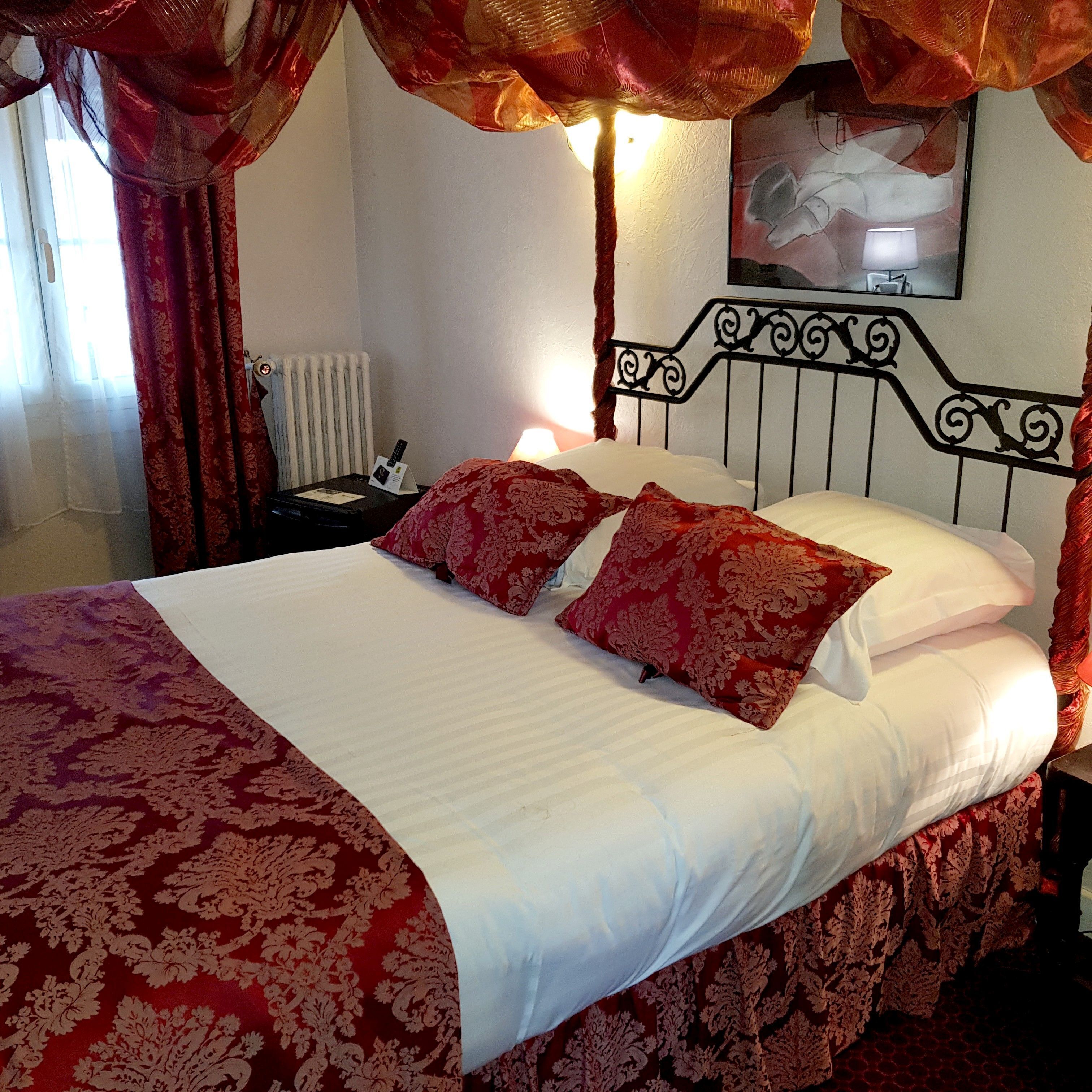 A bed with red and white bedding, a bedside table with a lamp, and a radiator.