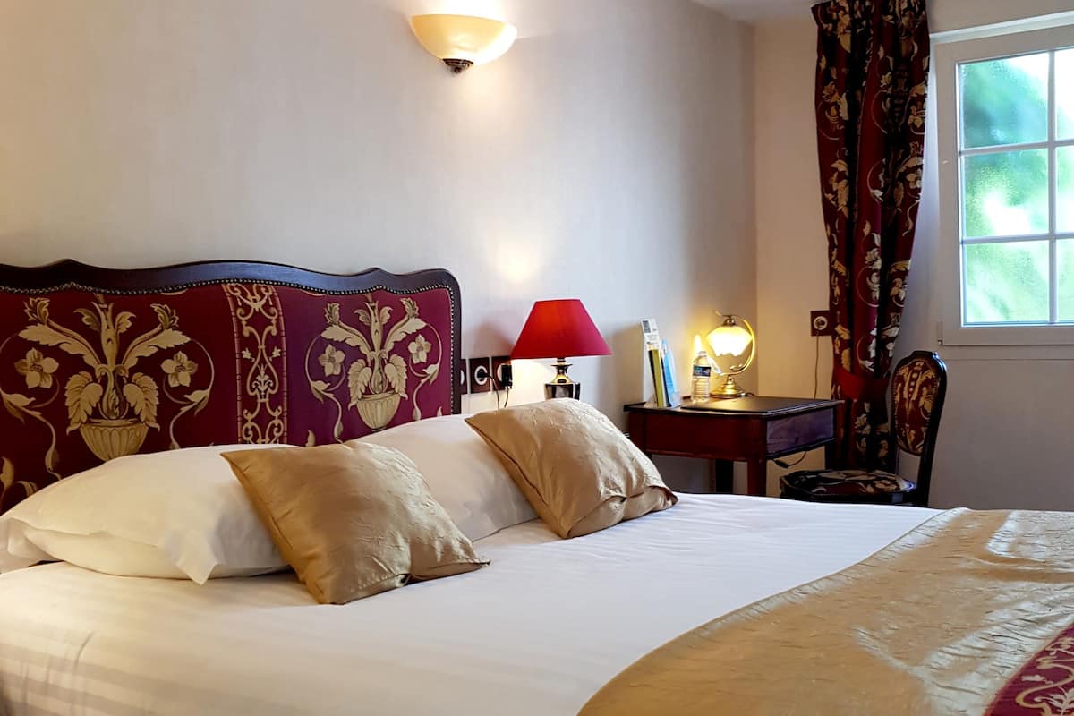 A neatly made bed with a headboard, a bedside table with a lamp, and a window with curtains.