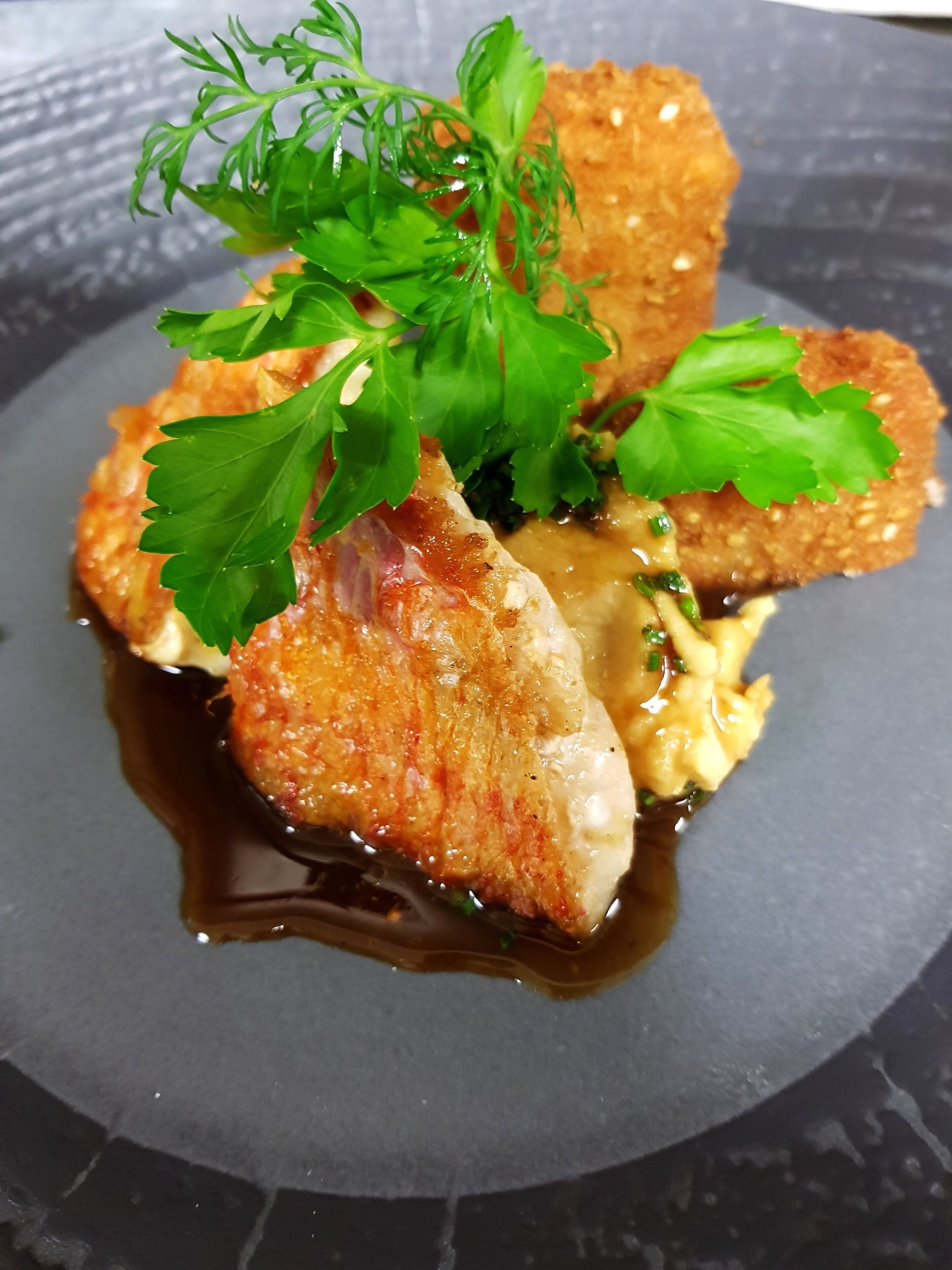 A plated dish with breaded items, sauce, and garnishes.