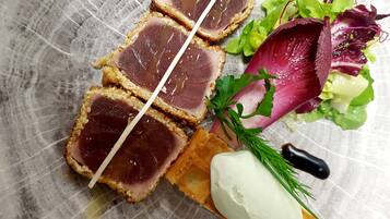 Un plato con carne en rodajas, una cucharada de crema y una ensalada de hojas.
