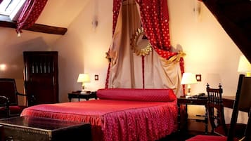 Un dormitorio con cama con dosel, dos mesitas de noche con lámparas, un baúl de madera y un espejo en la pared.