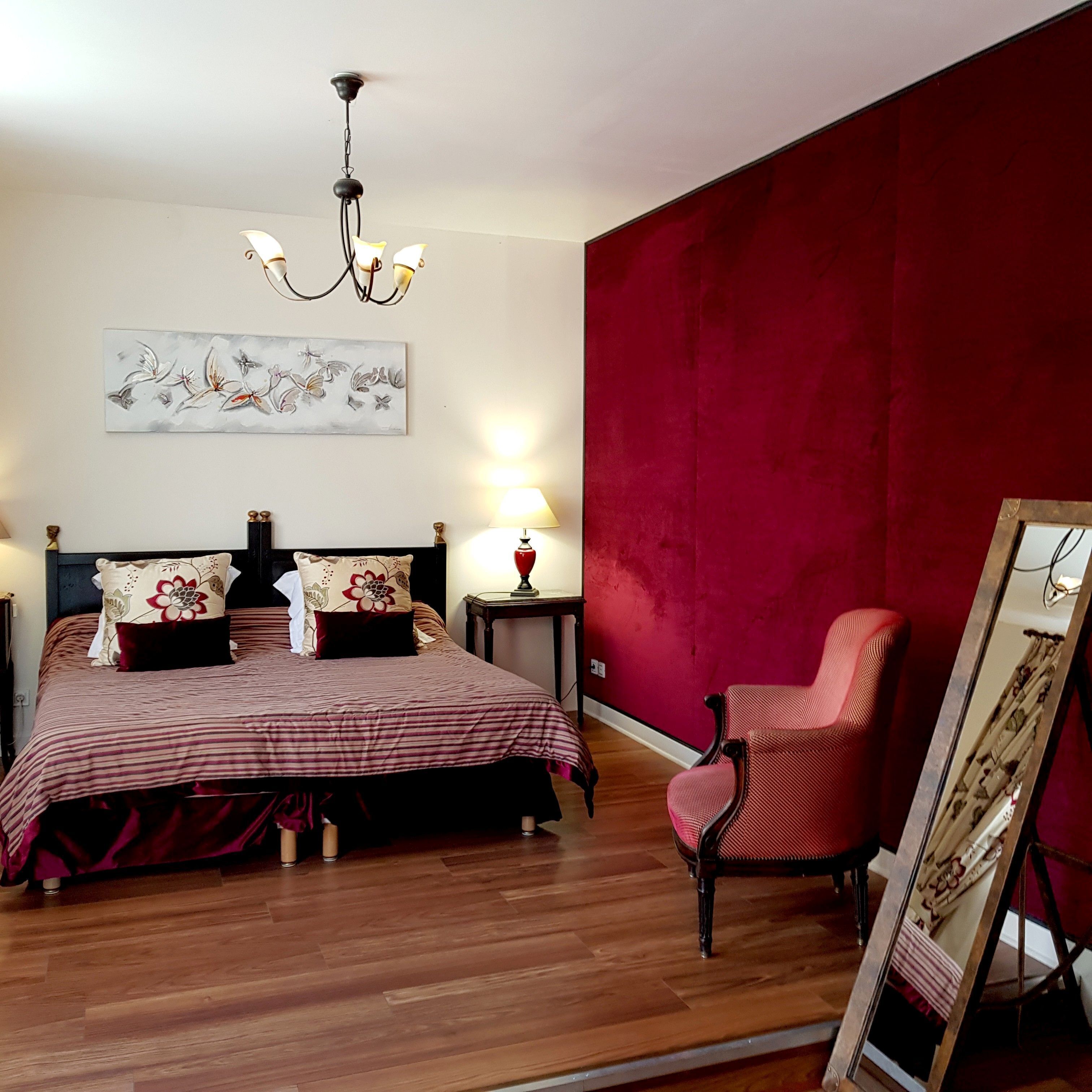 Quarto com cama, poltrona, abajur, pintura e parede vermelha.