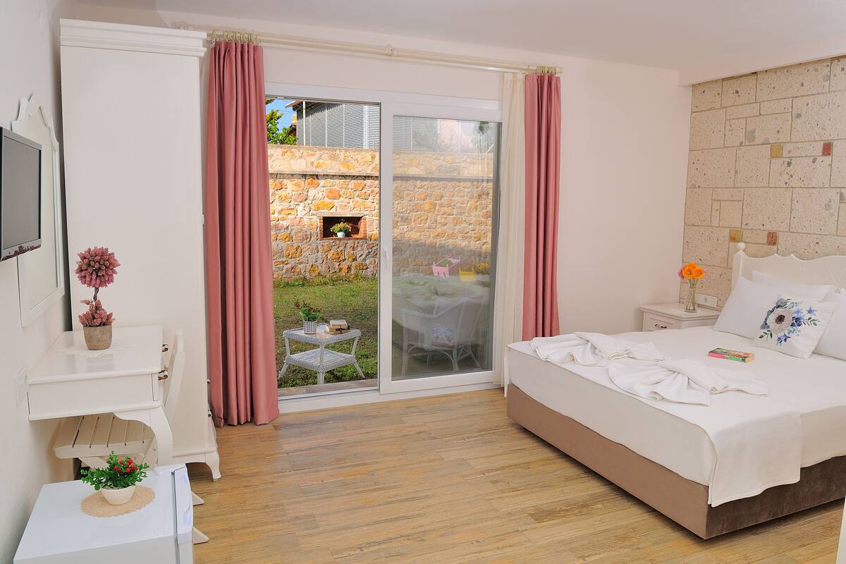 A bedroom with a bed, a desk, a chair, a small table with a plant, and a sliding glass door leading to an outdoor area.