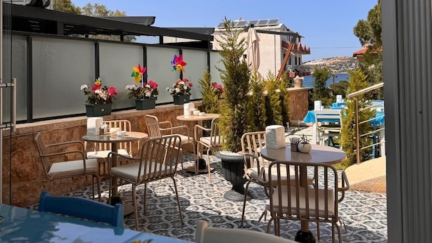 An outdoor patio with round tables and chairs, potted plants, and a view of the cityscape. - Allegria Hotel (Cesme)
