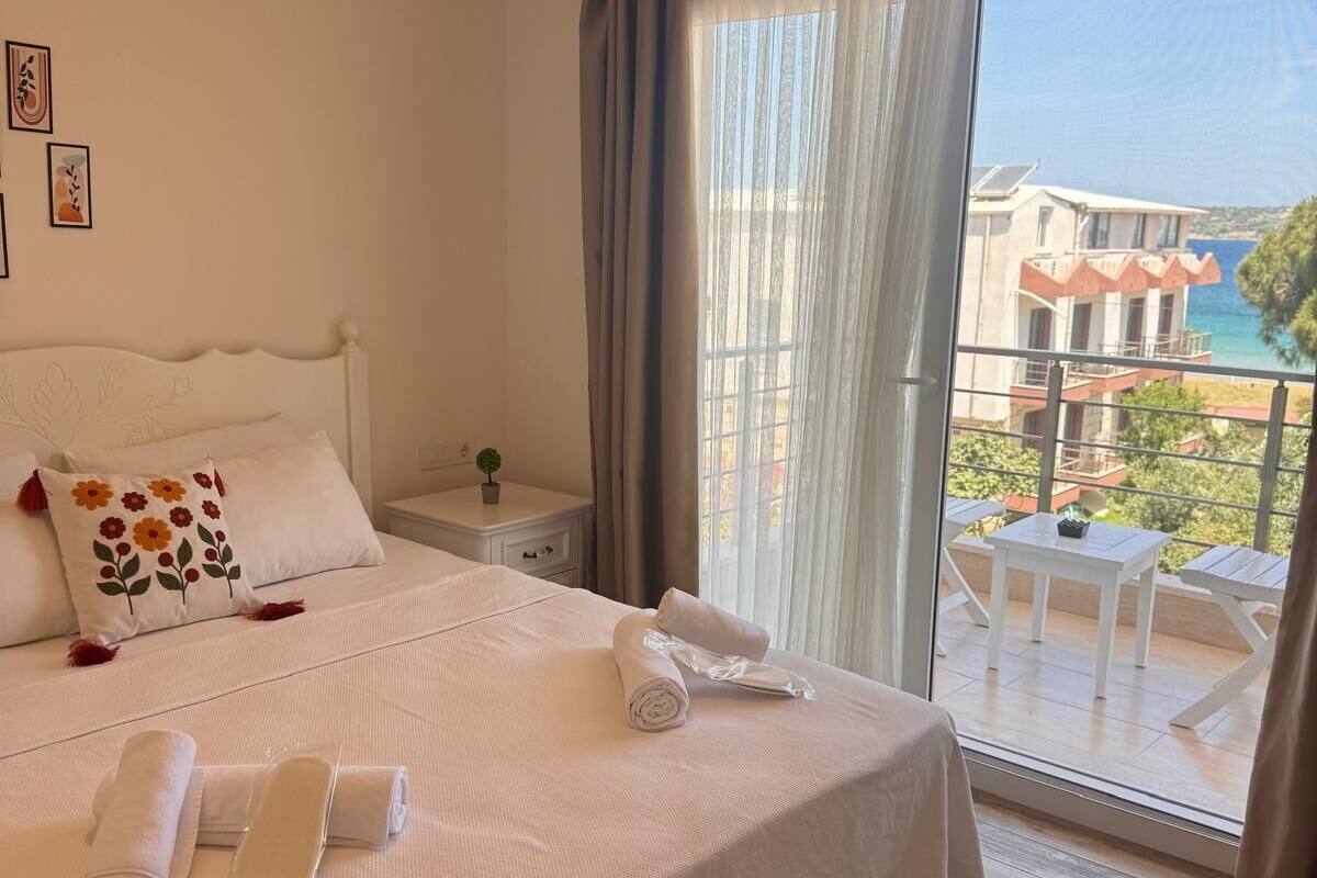 A hotel room with a large bed, a small bedside table, a potted plant, and a view of the sea through a balcony.