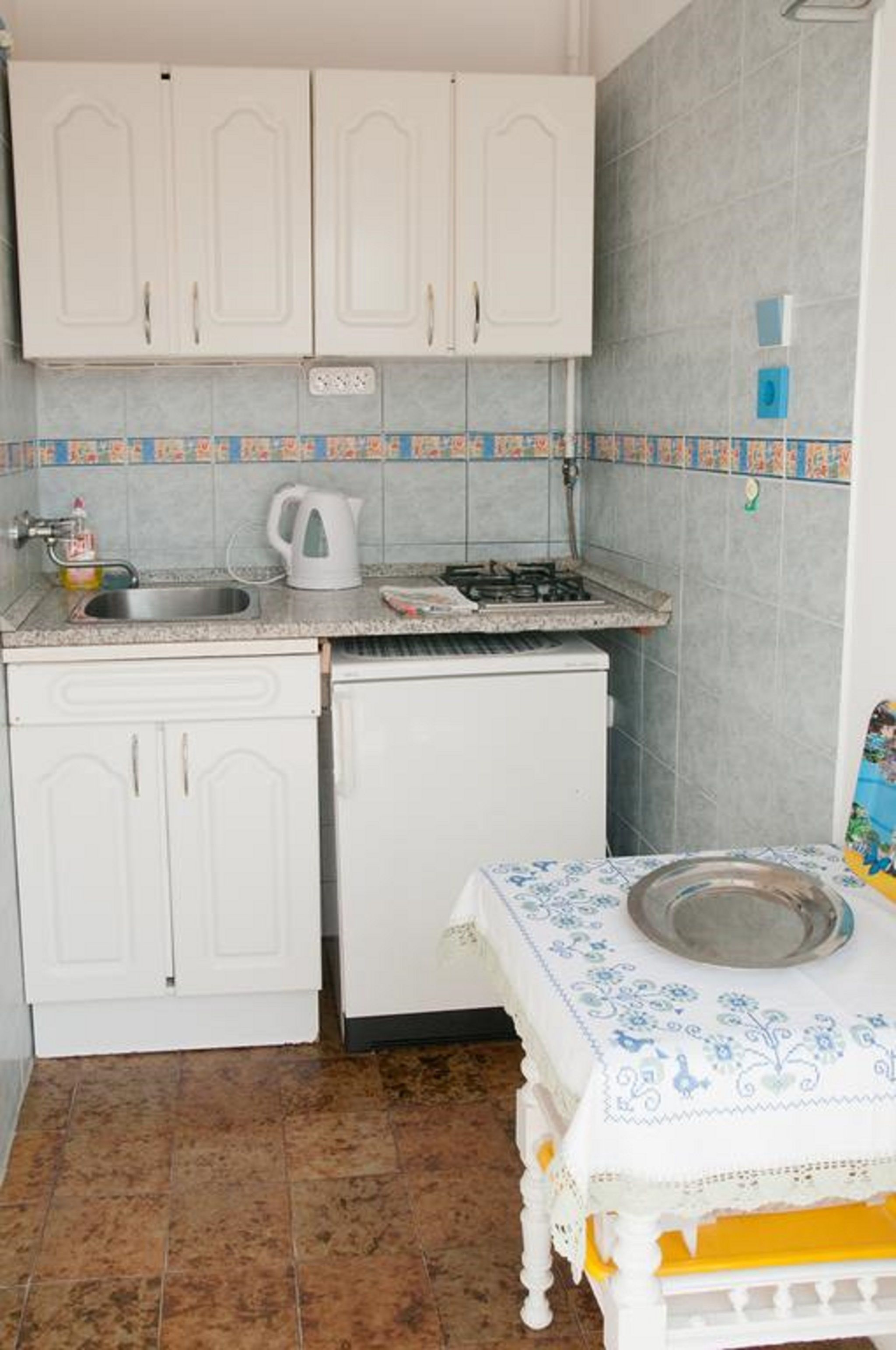Una cocina compacta con muebles blancos, un lavamanos pequeño y una estufa a gas.