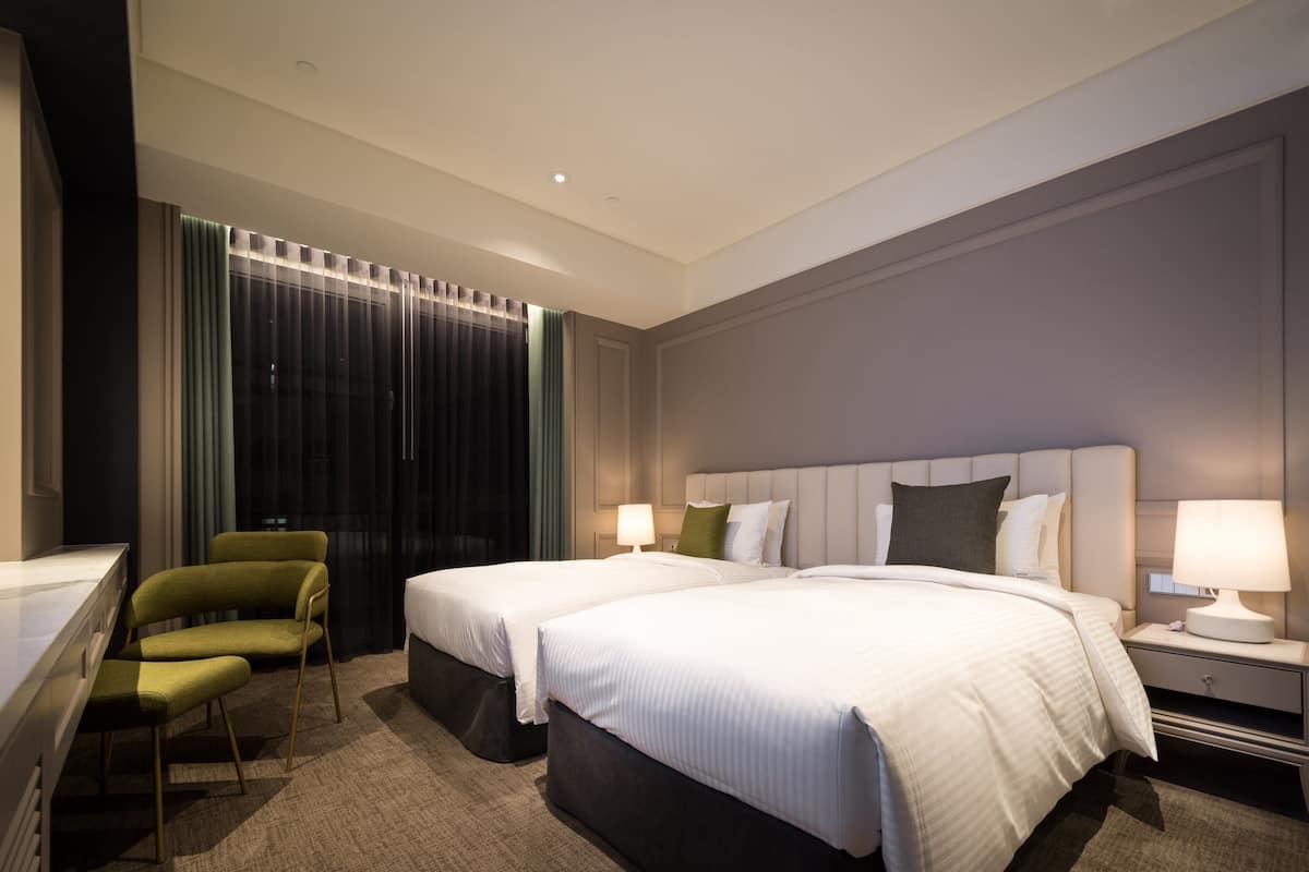A hotel room with two beds, a desk, and a chair.