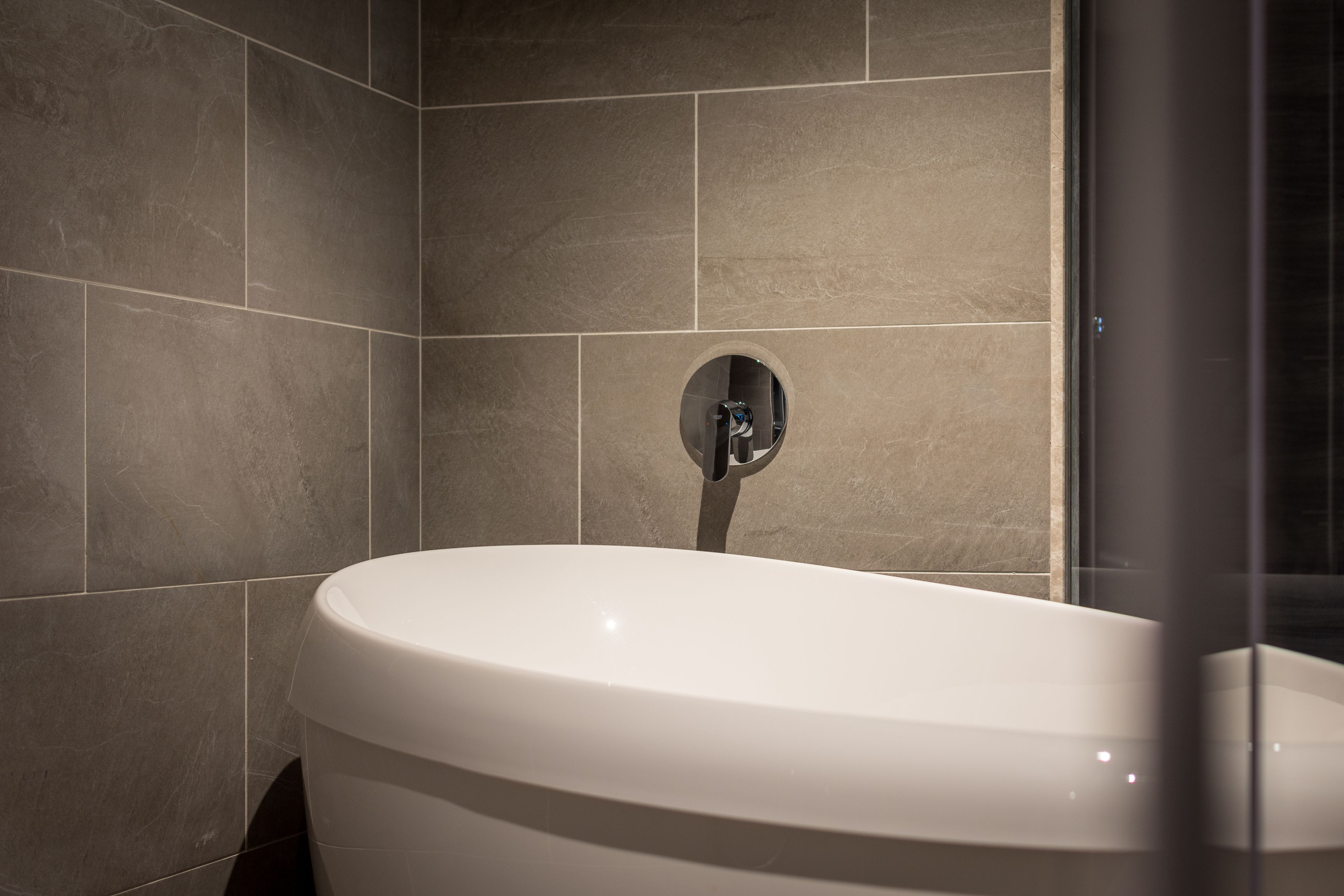Une salle de bain moderne avec une baignoire sur pieds, des murs carrelés et une douche à parois de verre.