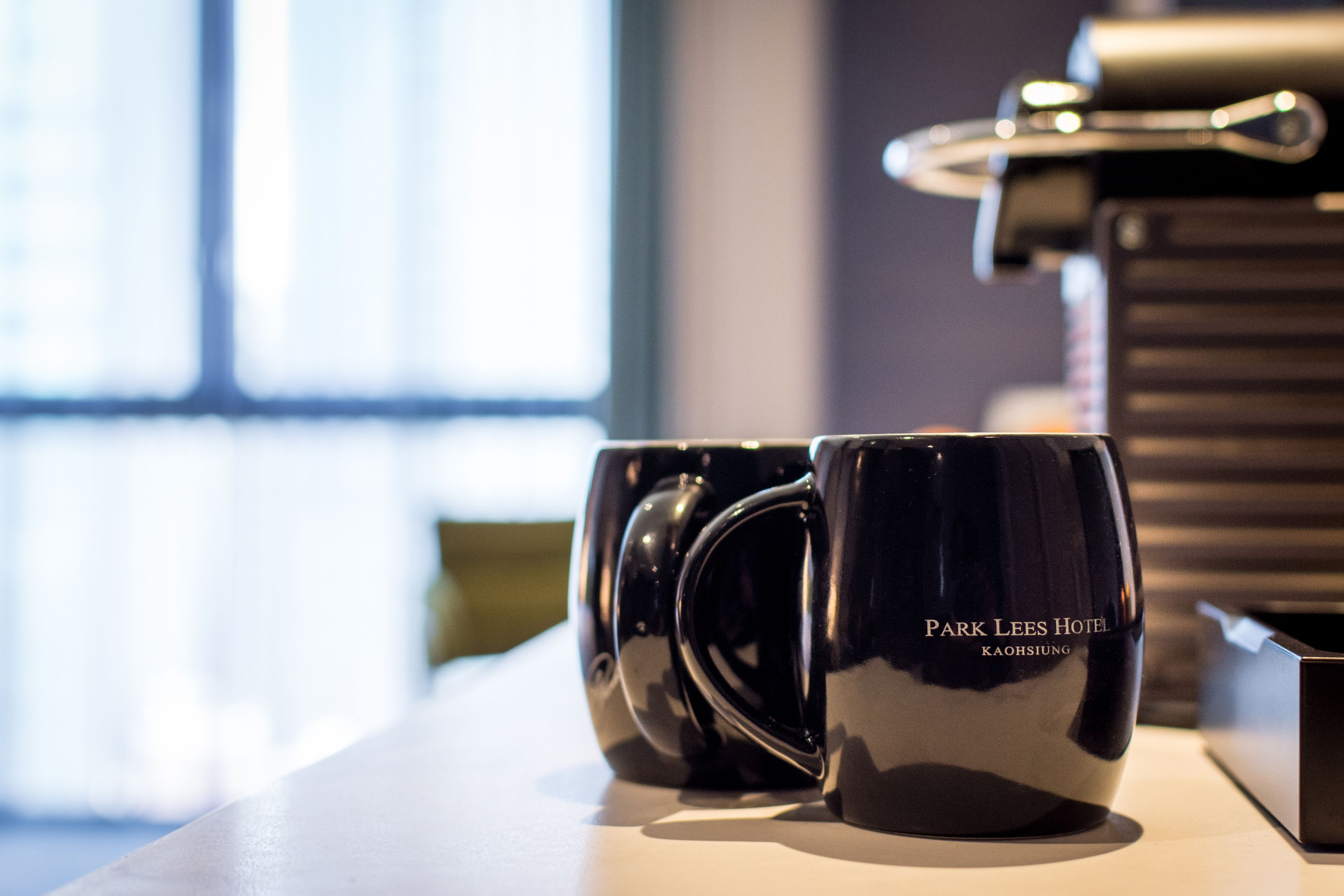 Two black mugs with the text "Park Lees Hotel Kaohsiung" on a table.