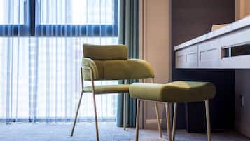 Una habitación moderna con una butaca y reposapiés tapizados en verde, un ventanal con cortinas translúcidas y una pared oscura con paneles de madera.