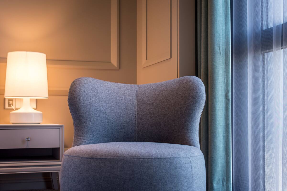 A modern armchair in a hotel room with a bedside table and lamp.