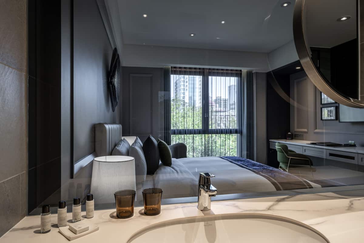 A modern hotel room with a large bed, a desk, and a bathroom with a marble sink.