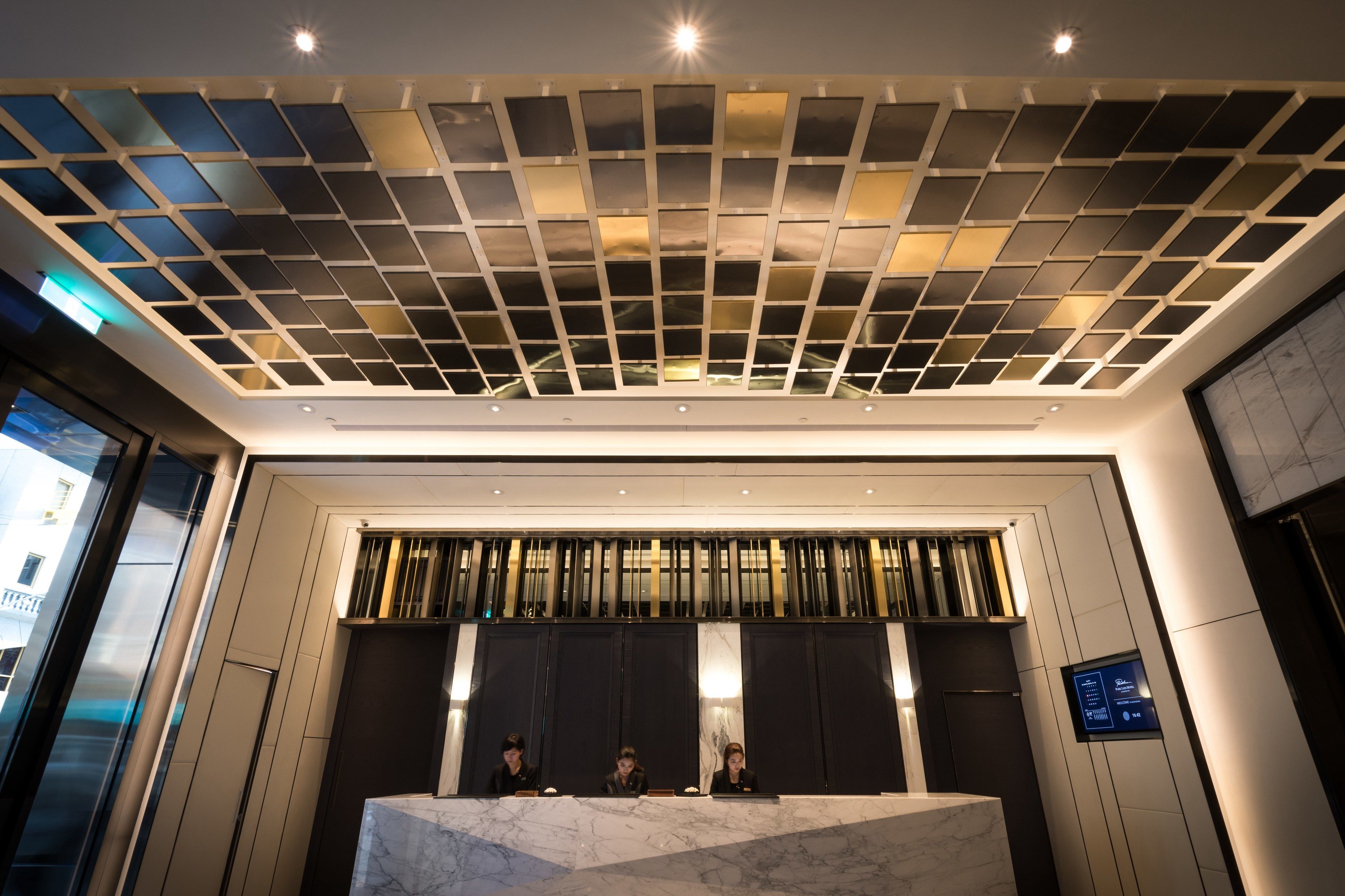 A reception desk with a marble top, a modern ceiling design, and a digital display.