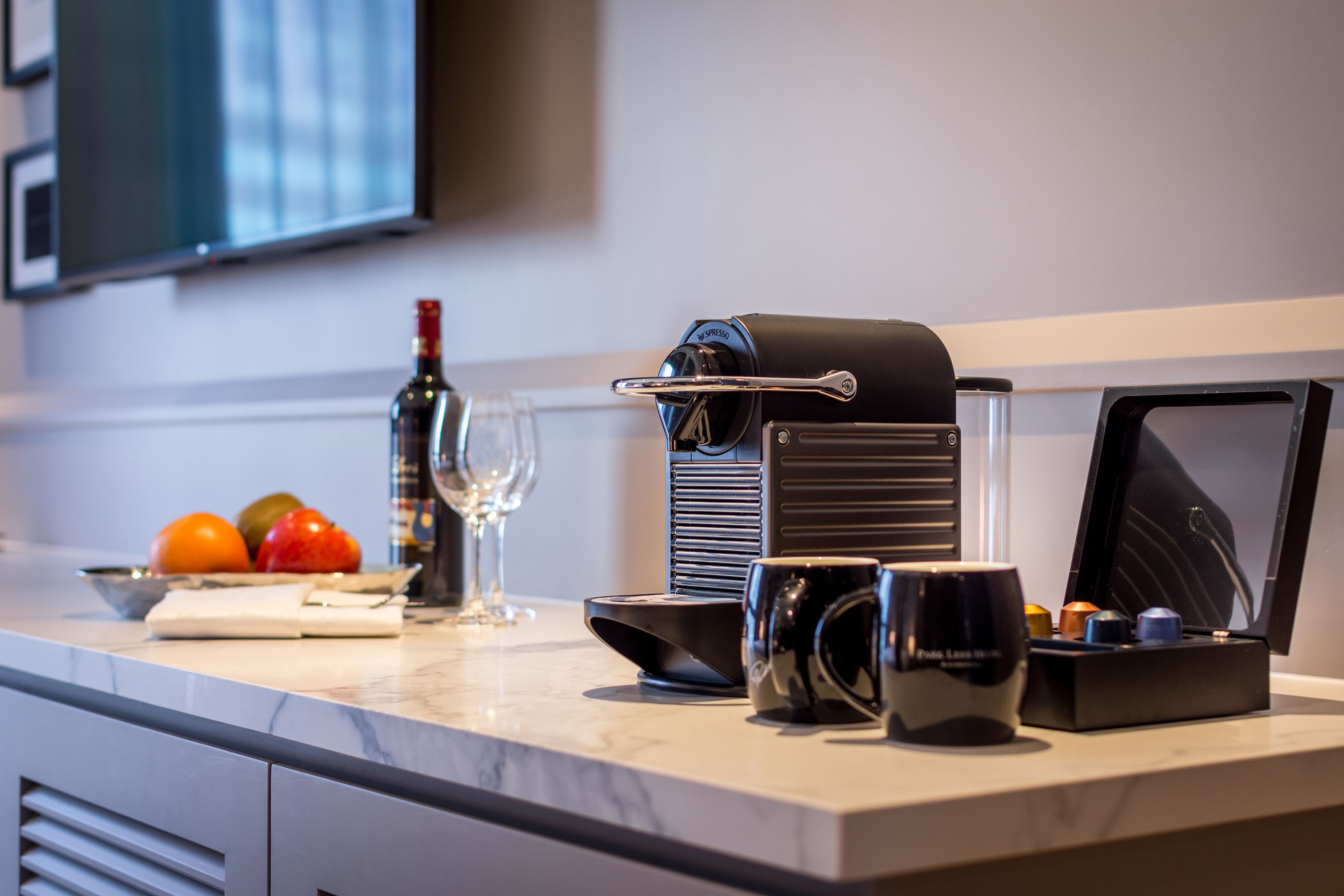 A modern kitchen with a coffee machine, a wine bottle, and fresh fruit on the counter.