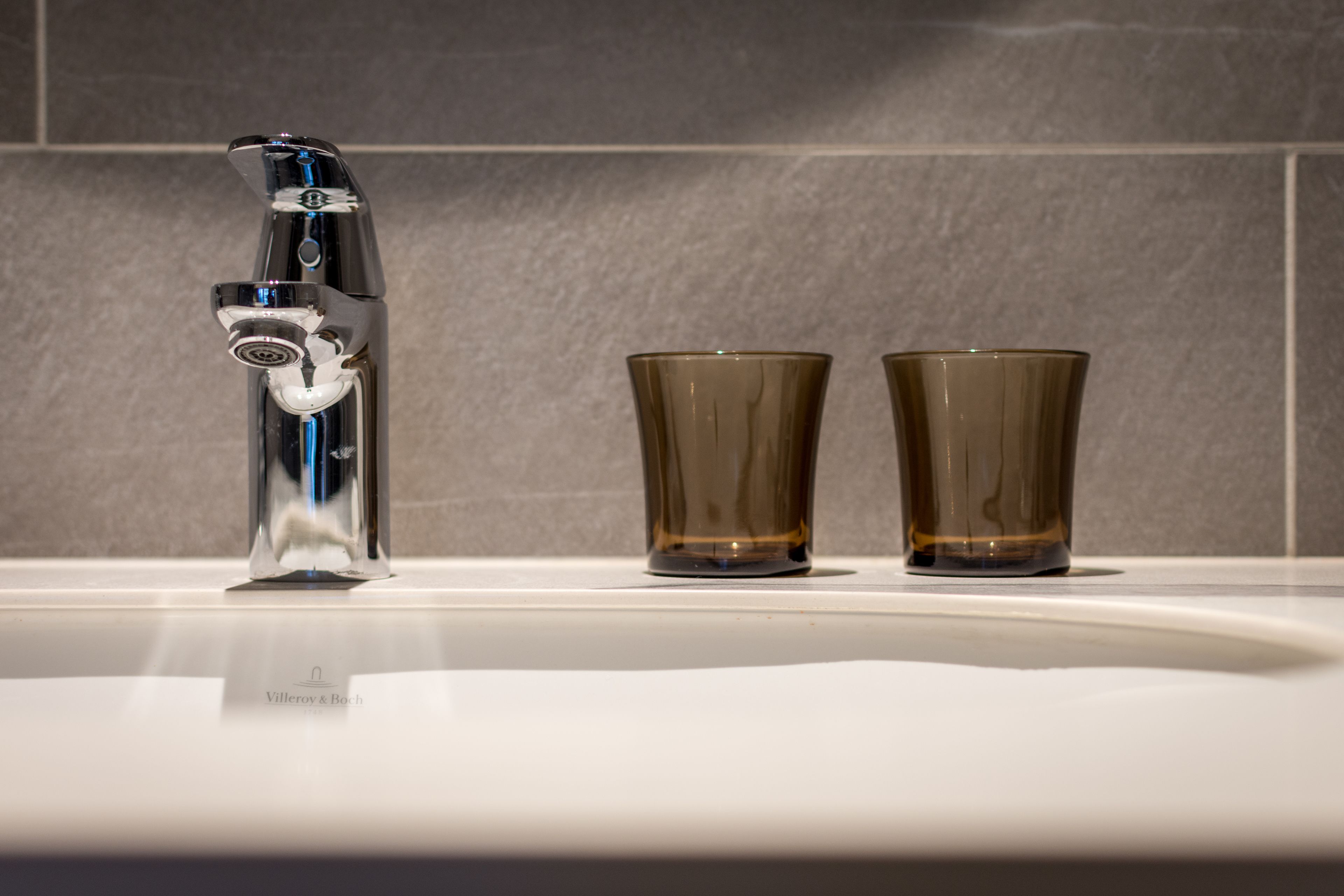 A bathroom sink with a modern faucet and two clear glasses.