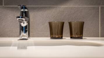 A bathroom sink with a modern faucet and two clear glasses.