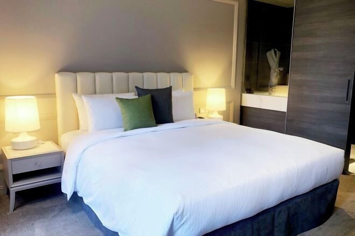 Una cama bien hecha con ropa de cama blanca, dos lámparas de noche y un cabecero oscuro.
