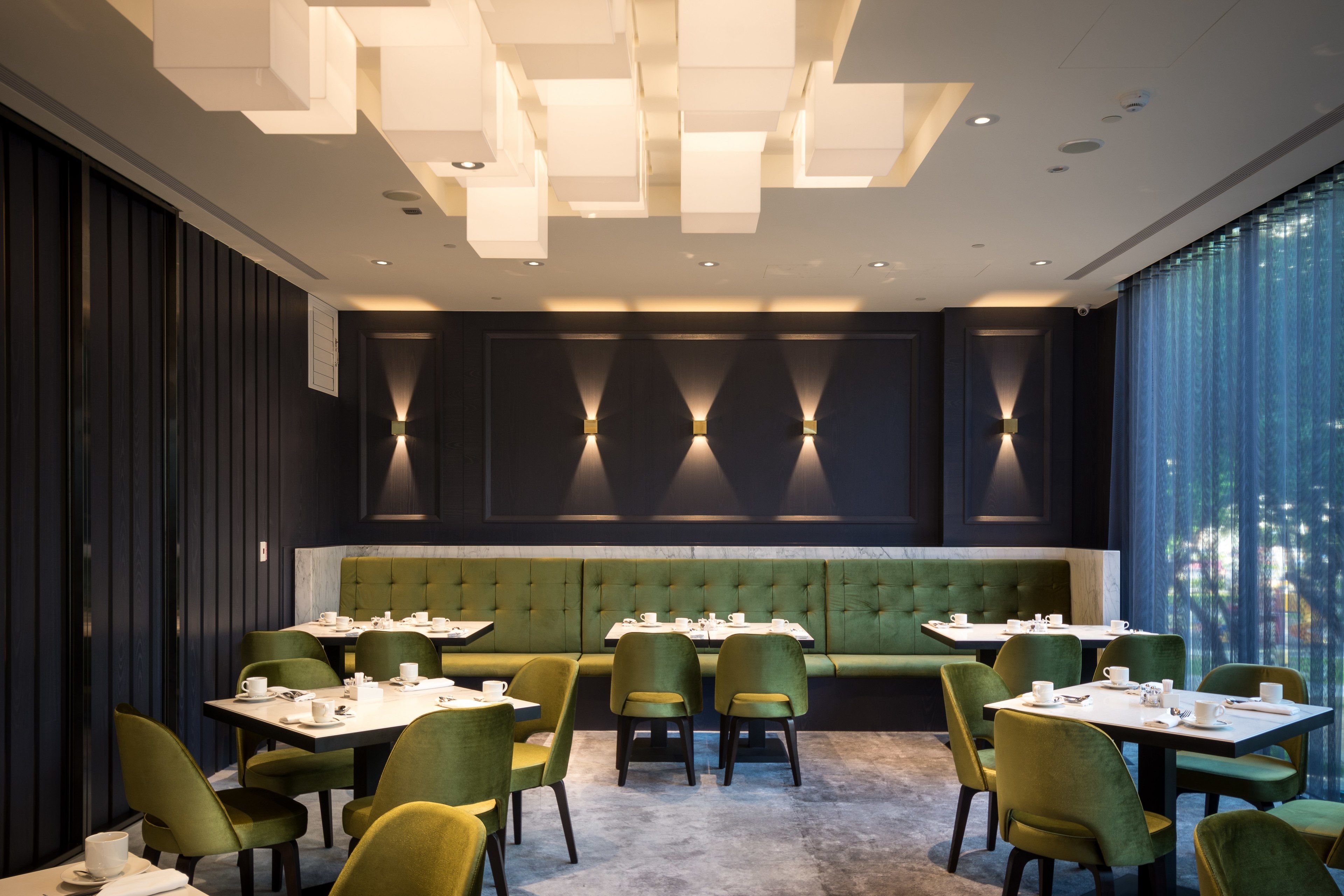 A restaurant with green upholstered booths, green chairs, and white tables.
