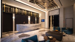 Un moderno vestíbulo de hotel con un mostrador de recepción de mármol, zona de estar y una gran pantalla digital.