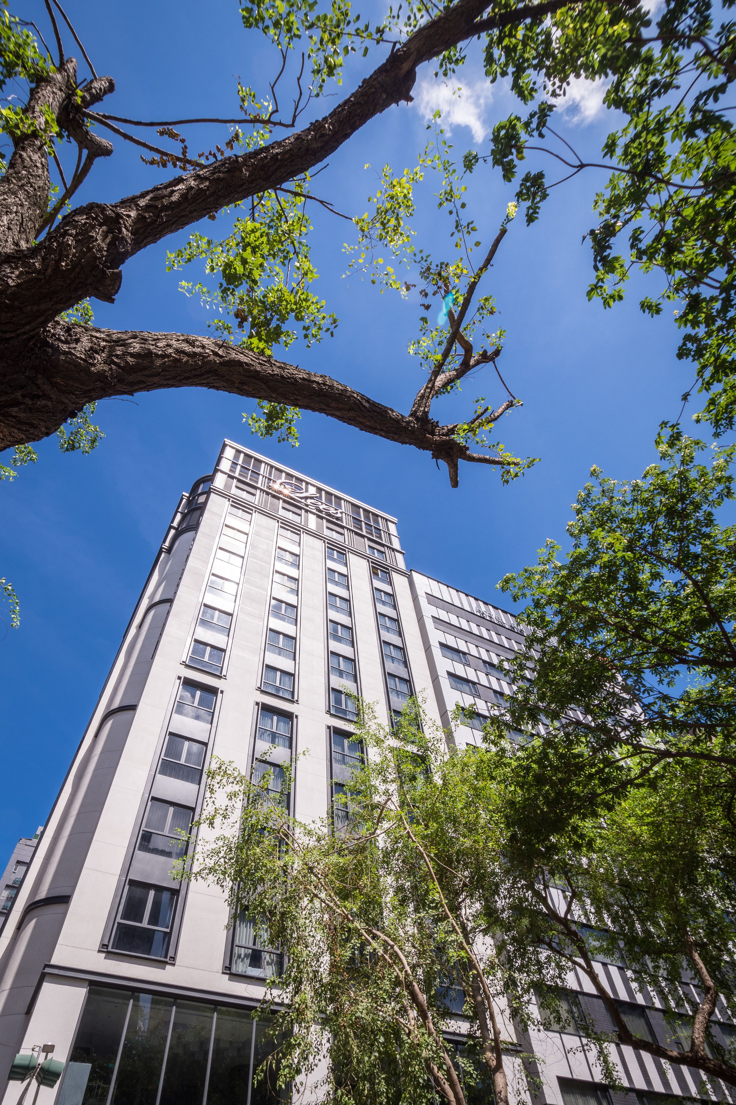 A tall building with multiple floors and large windows, surrounded by trees and greenery.