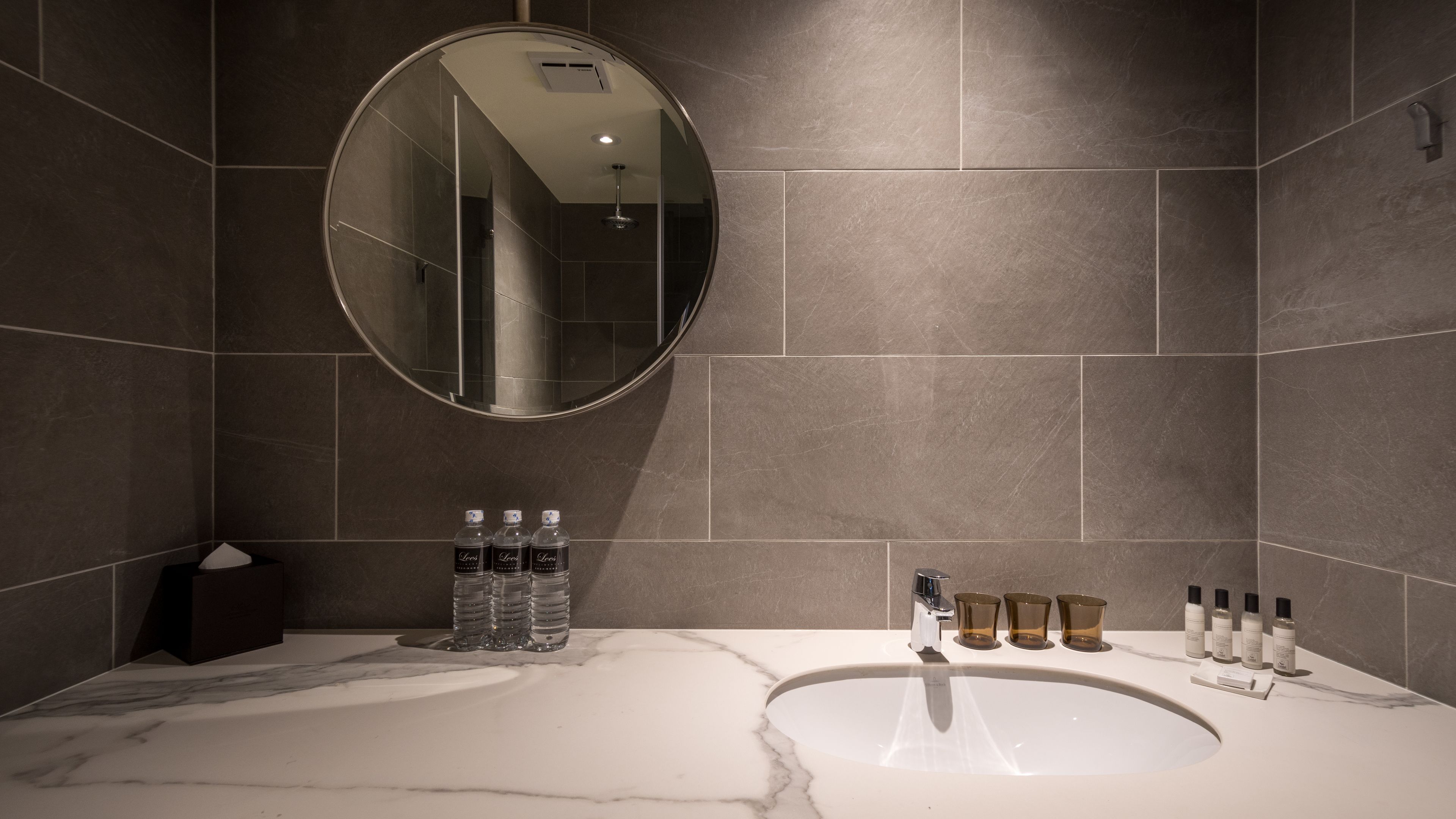 A modern bathroom with a marble sink, a large mirror, and toiletries on the counter.