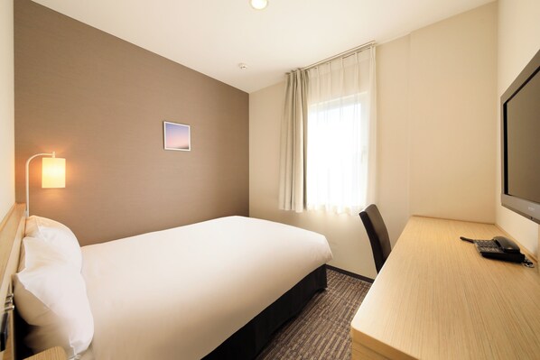 Una habitación de hotel con cama, escritorio, silla, lámpara, televisión y ventana con cortinas.
