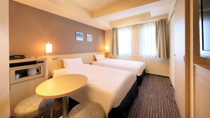Une chambre d’hôtel avec deux lits, une petite table, une chaise, un bureau avec une lampe et un téléviseur.