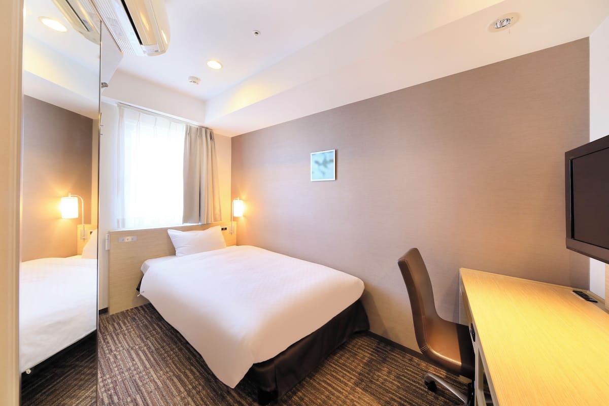 A hotel room with two single beds, a desk, a chair, a television, and a window with curtains.