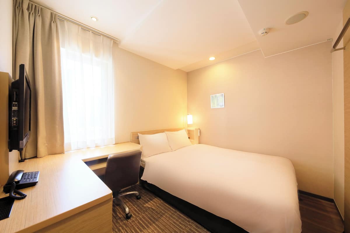 A hotel room with a bed, a desk, a chair, a television, and a window with curtains.