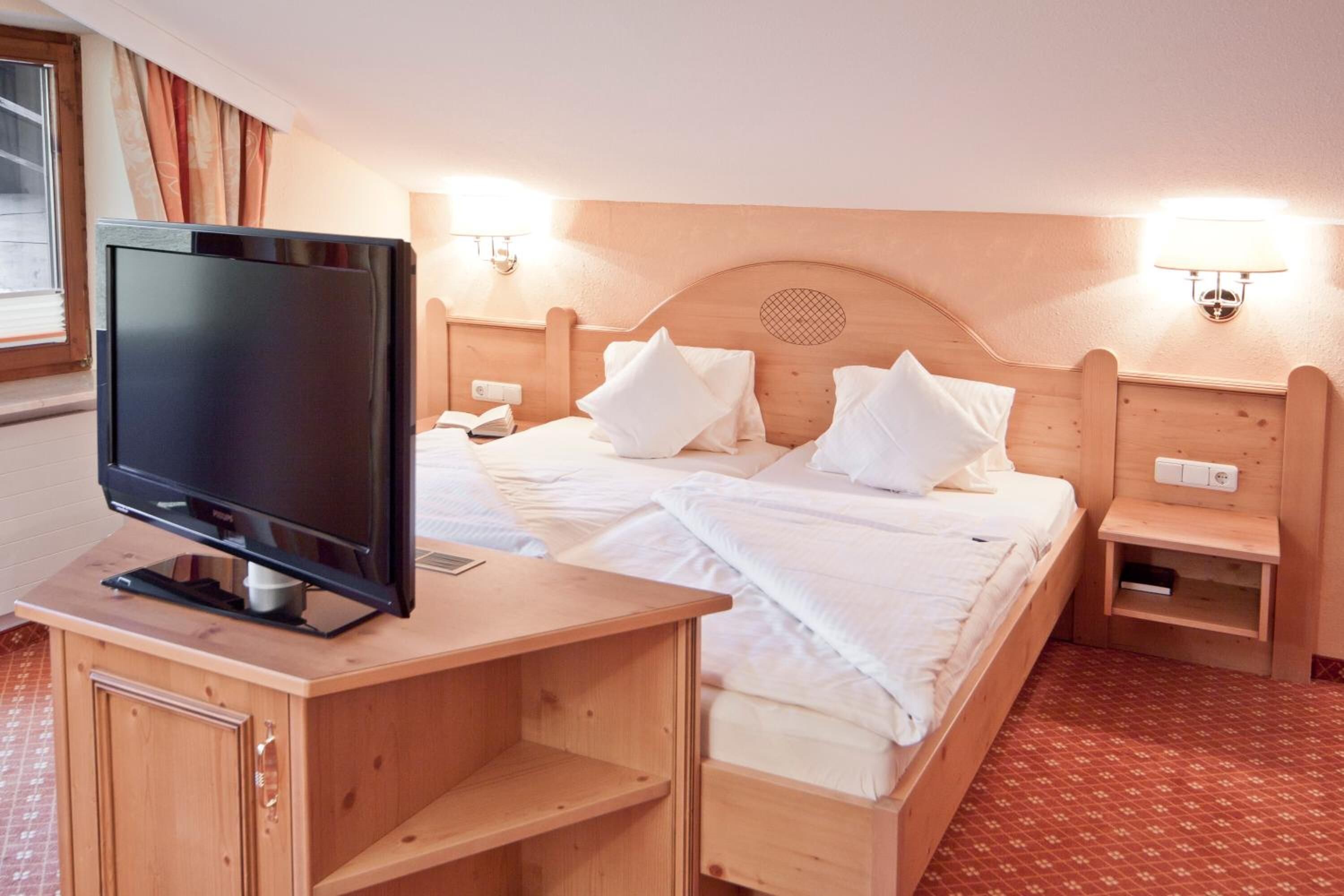 Ein Hotelzimmer mit einem hölzernen Bett, einem Fernseher auf einem Holzständer und zwei Nachttischlampen.