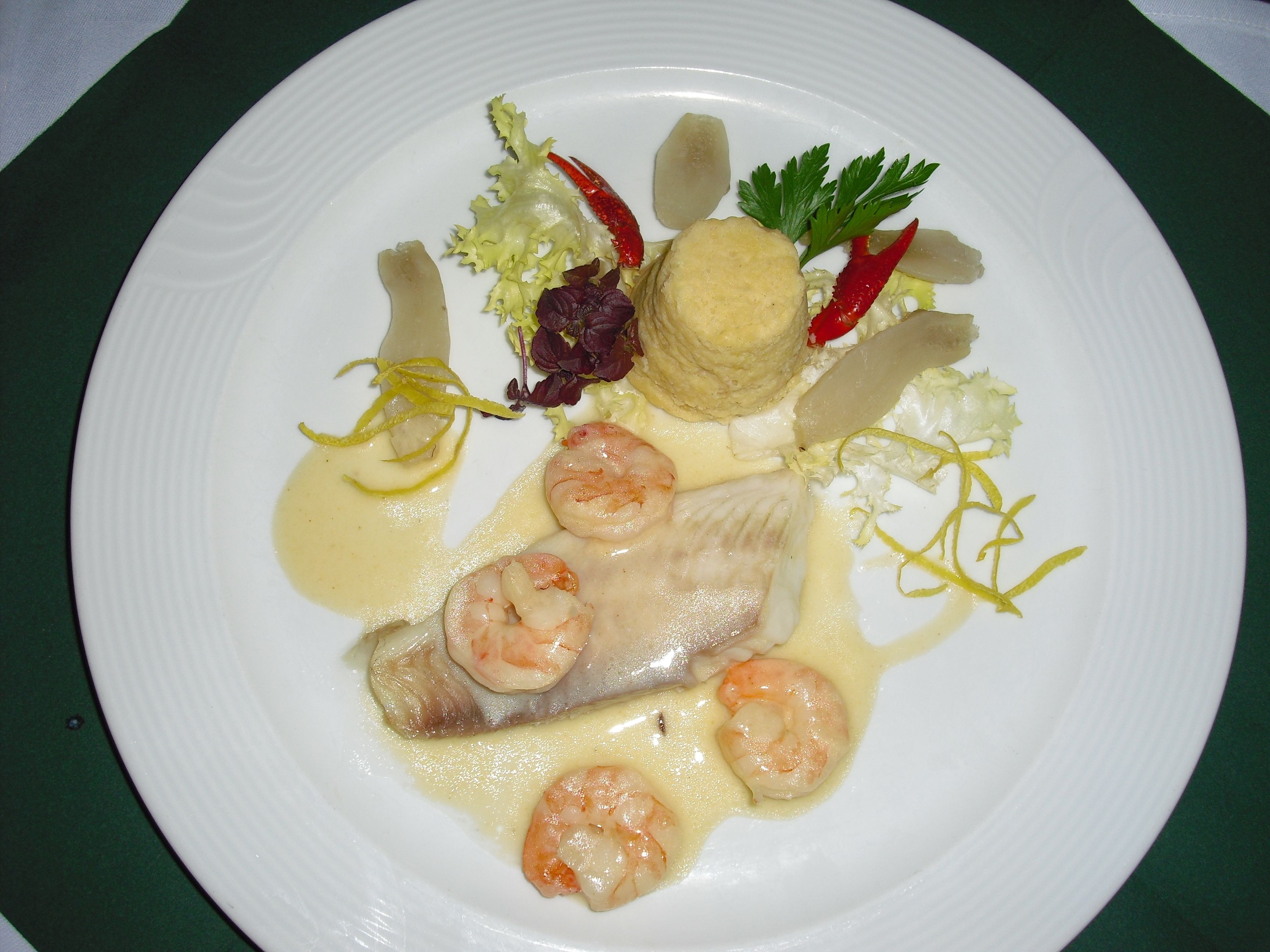 A plate with seafood, including shrimp and fish, served with a creamy sauce and garnishes.