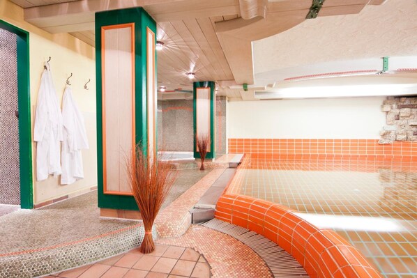 A spa area with a tiled hot tub, a wall with hanging towels, and a decorative plant.