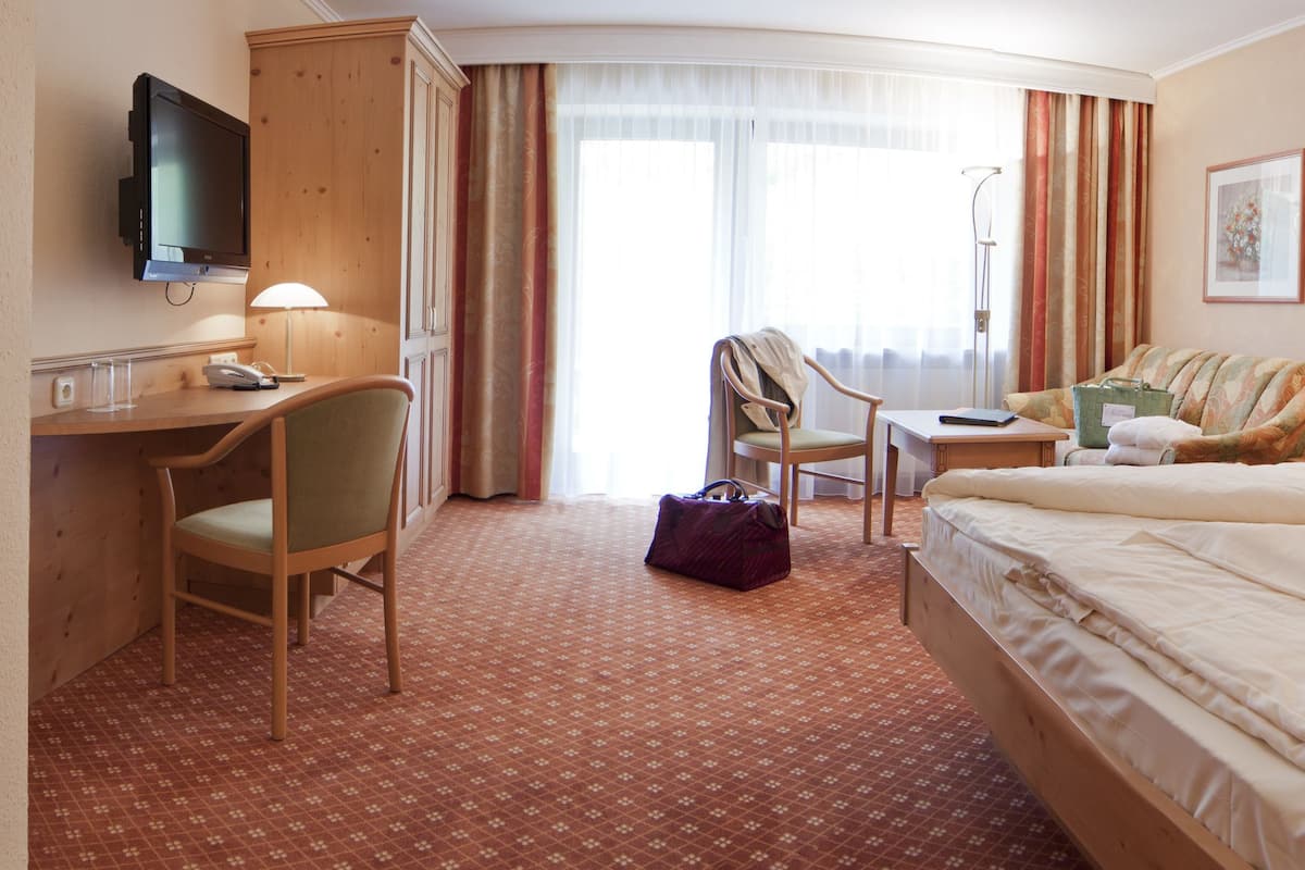 Ein Hotelzimmer mit Bett, Schreibtisch, Sessel, Sofa und Fernseher.
