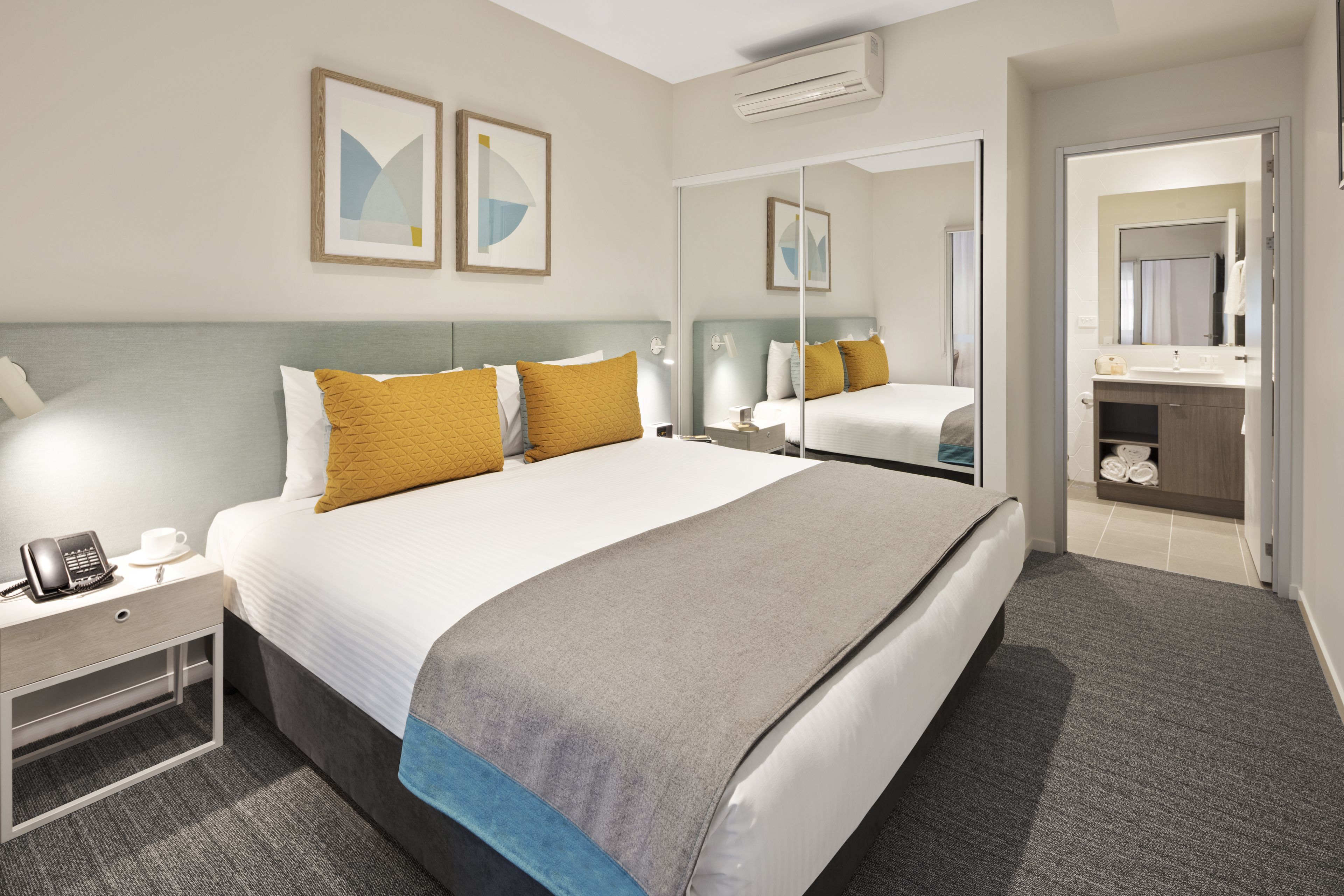 A modern hotel room with a large bed, bedside tables, a mirror, and a bathroom visible through an open door.