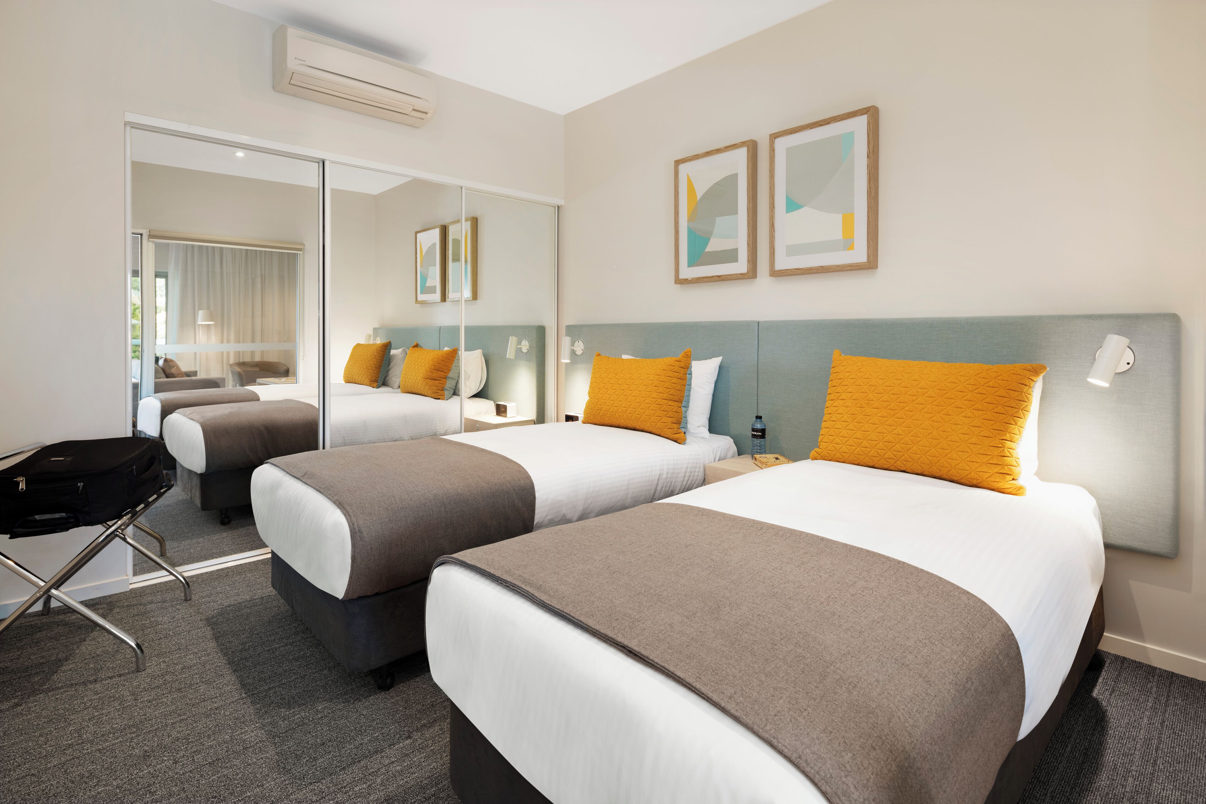 A hotel room with two beds, a large mirror, and artwork on the wall.