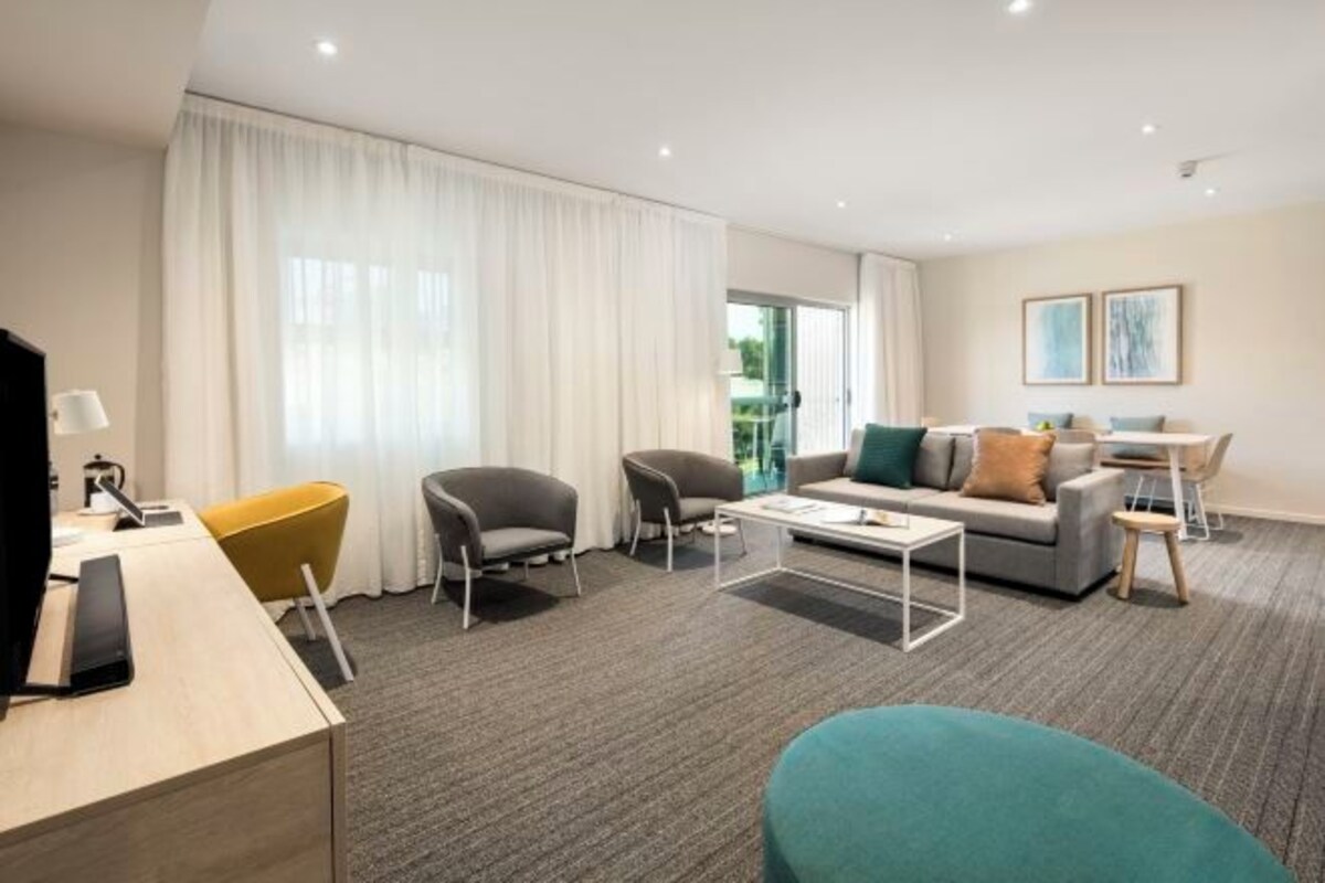 Una habitación de hotel moderna con un ventanal grande, un sofá, una mesita de centro y un escritorio con lámpara.