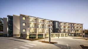 Um hotel de vários andares com design moderno, apresentando varandas, janelas amplas e uma entrada bem iluminada.