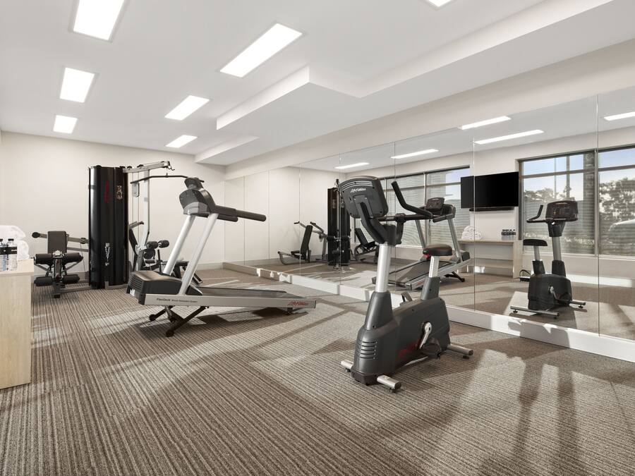 A modern gym with various cardio machines, a reception desk, and large windows offering natural light.