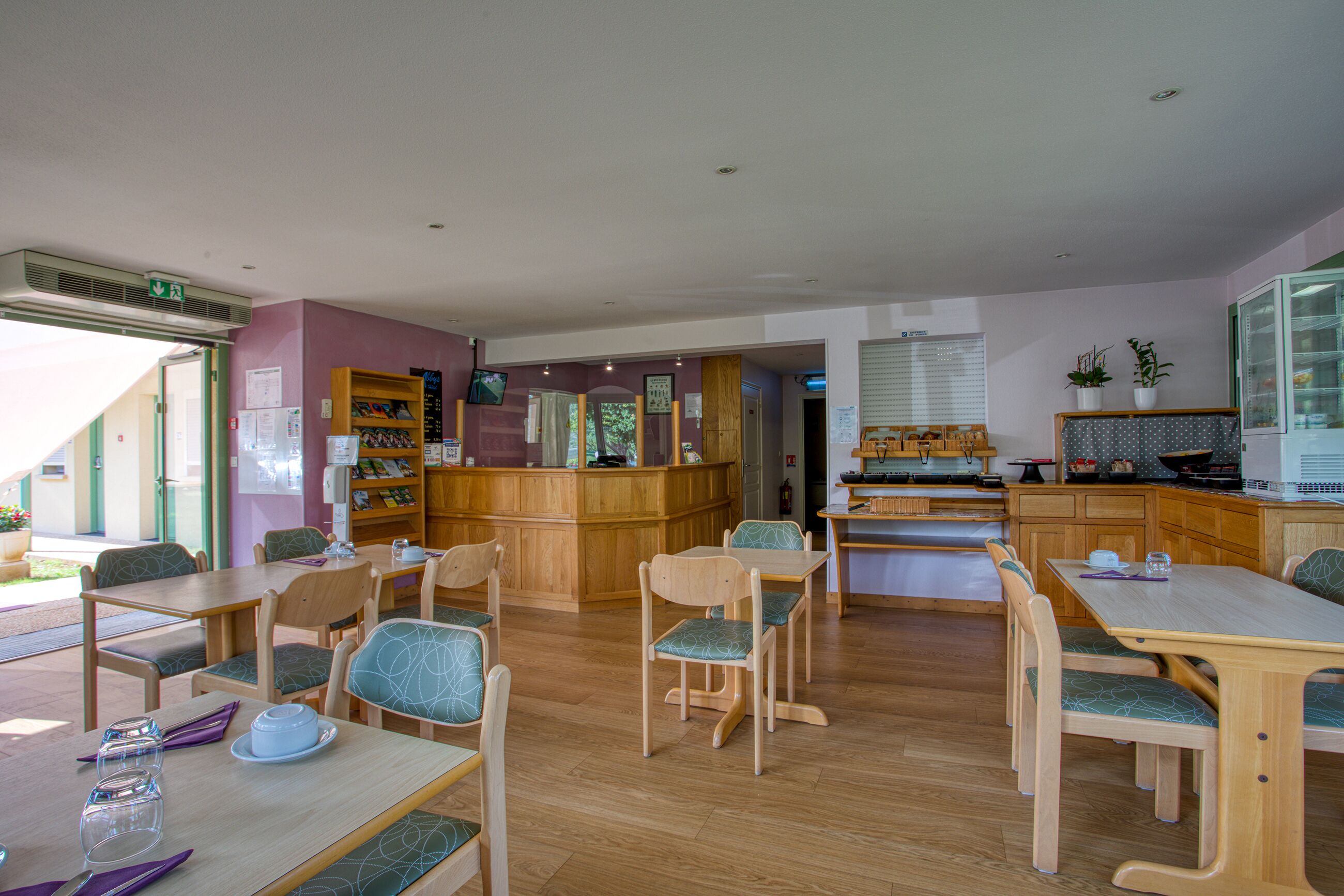 A dining area with wooden tables and chairs, a counter with a menu, and a kitchen area in the background.