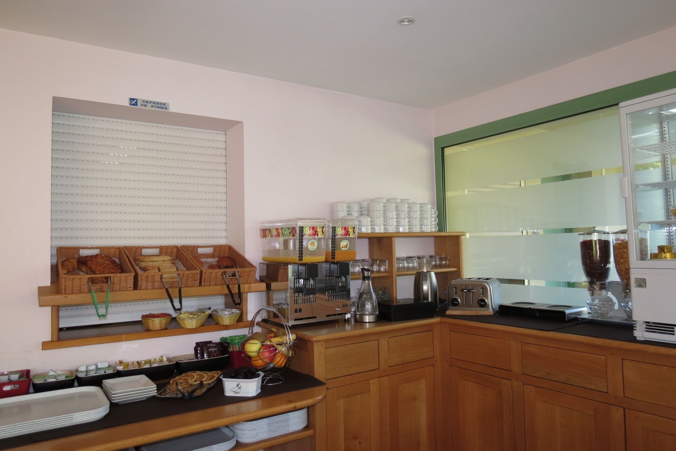 Una cocina con armarios de madera, una encimera con distintos alimentos, una cafetera y una ventana con persianas.