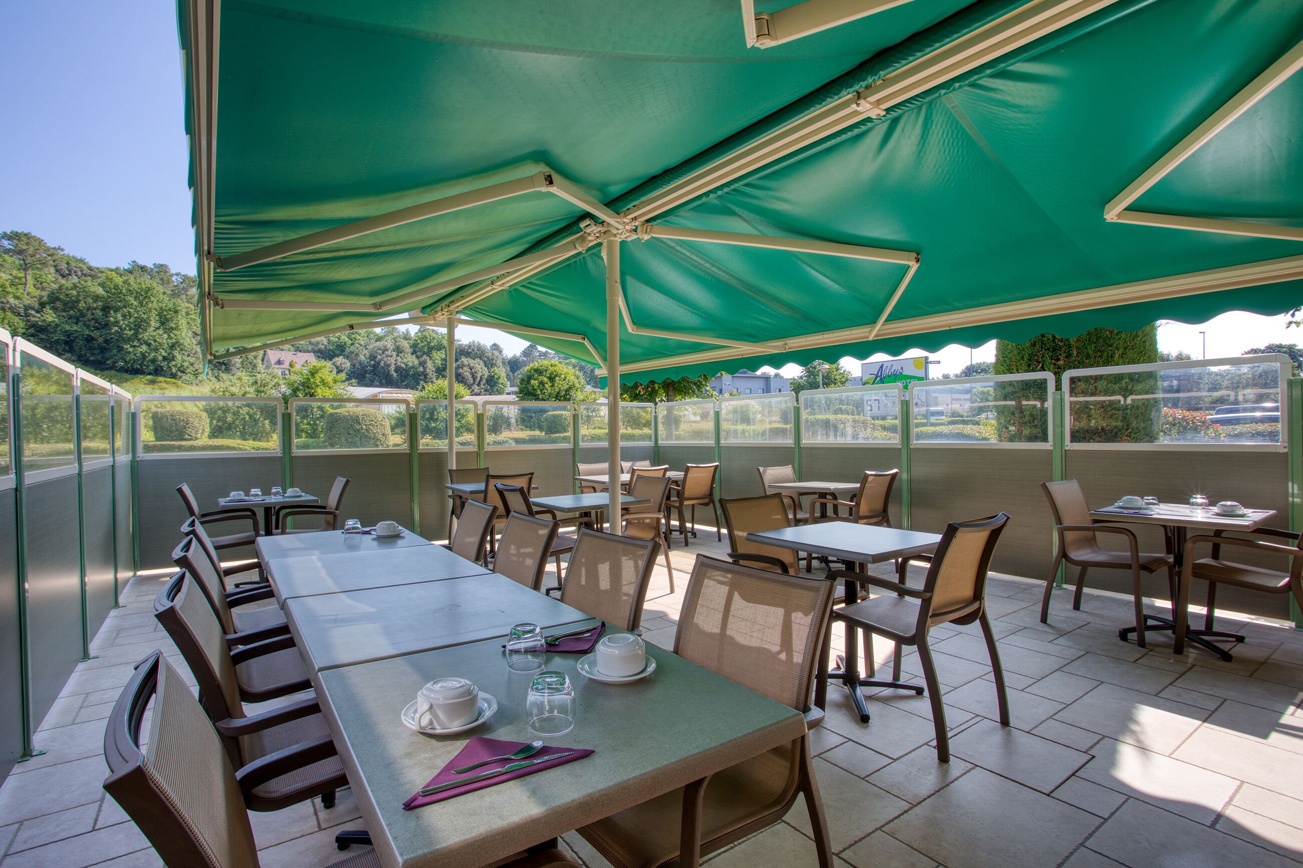 An outdoor patio area with tables and chairs under green canopies, overlooking a scenic landscape.