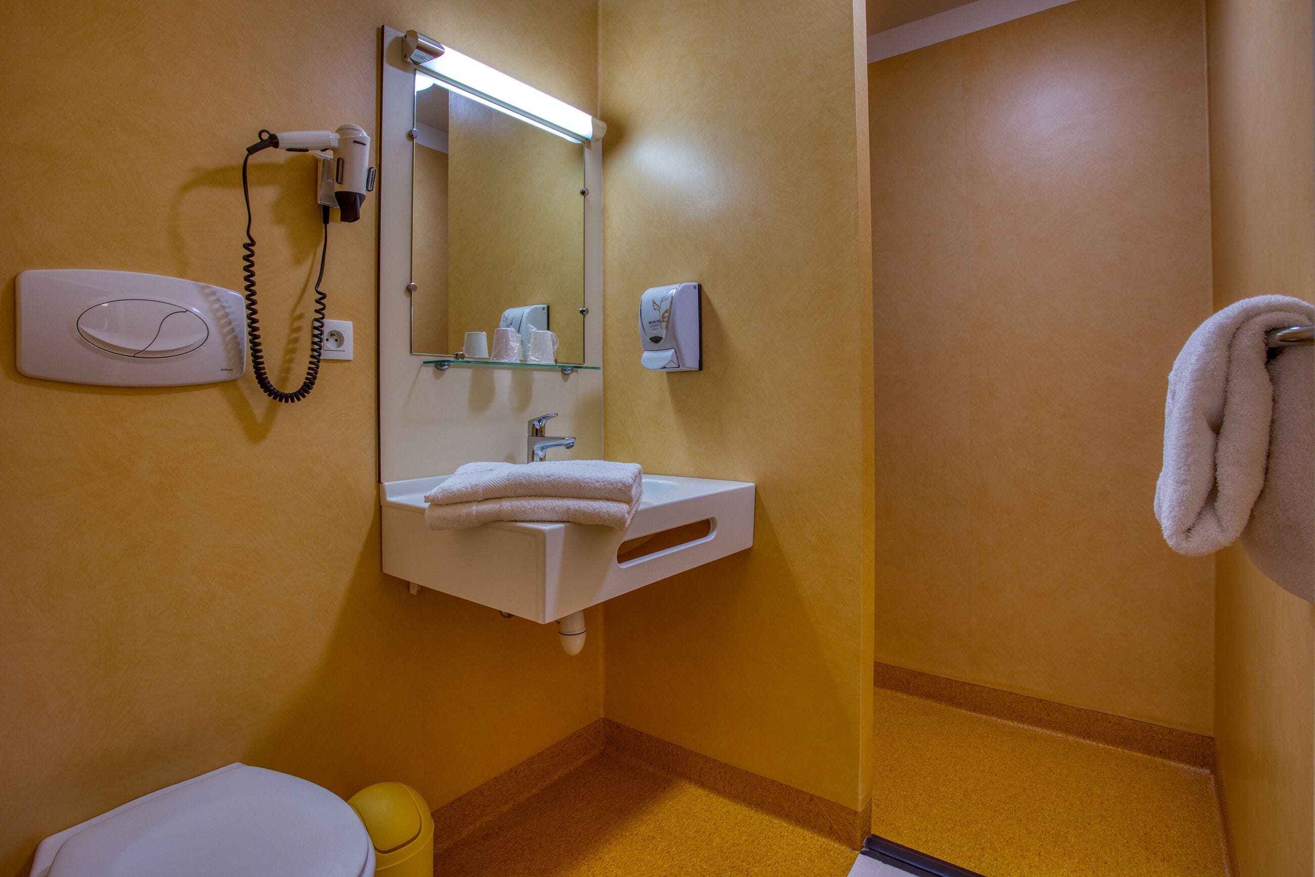 A bathroom with a white sink, a mirror, a hairdryer, a towel rack, and a toilet.