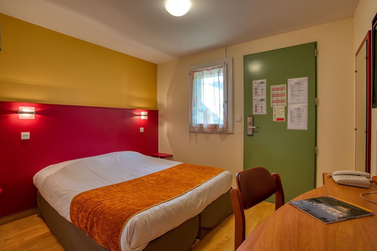 A hotel room with a bed, a desk with a telephone, and a chair.