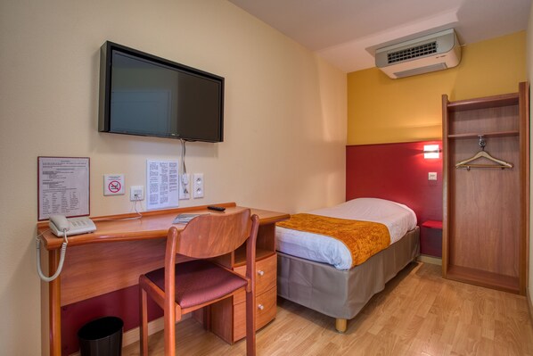 A hotel room with a wooden desk, a single bed, a television mounted on the wall, and a wardrobe. - Abbys Hôtel (Carsac-Aillac)