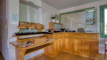 Una cocina con armarios de madera, estufa empotrada, pileta y ventana con persianas.