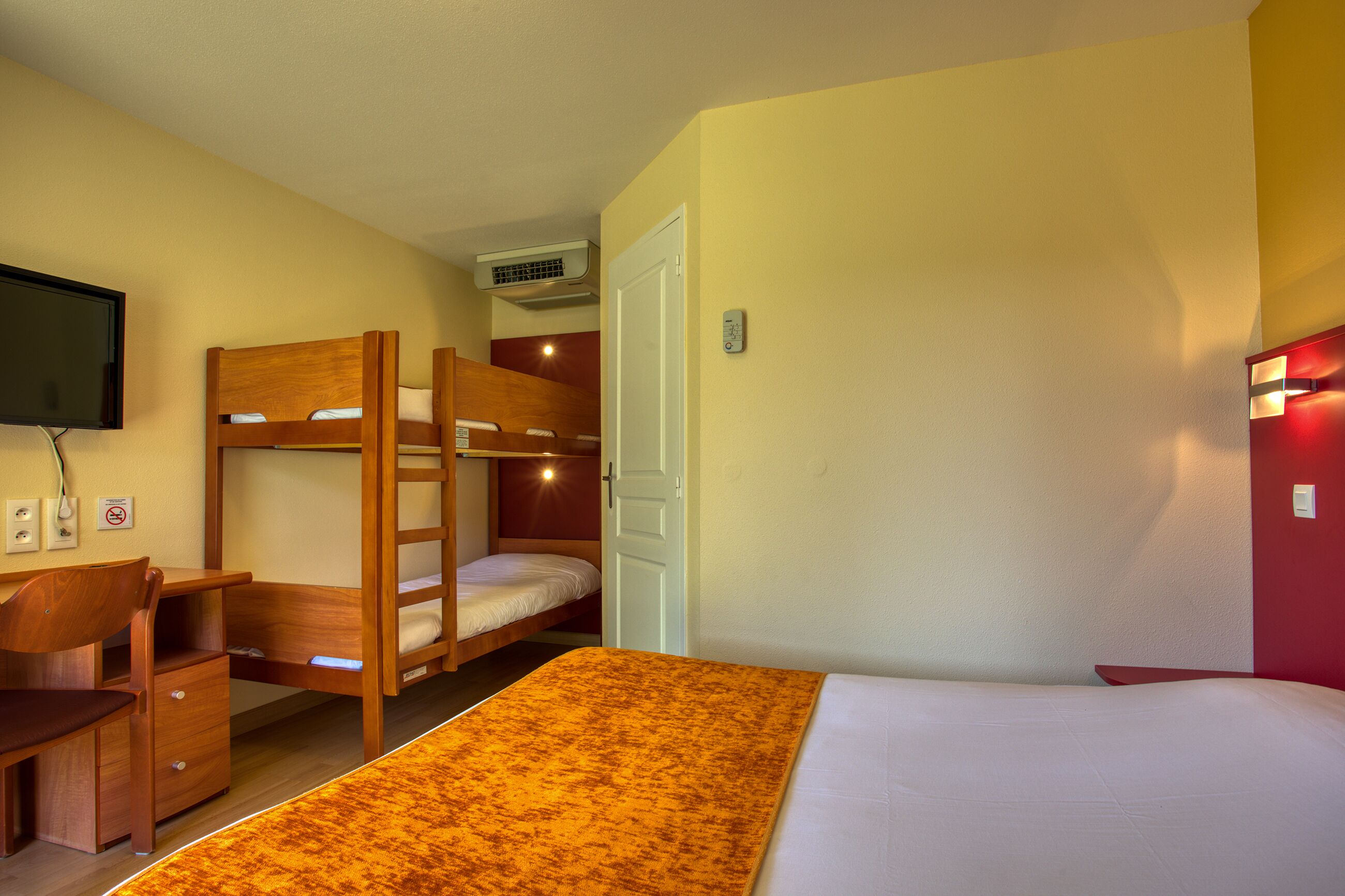 Habitación con literas, escritorio, televisor y una pared de acento roja.