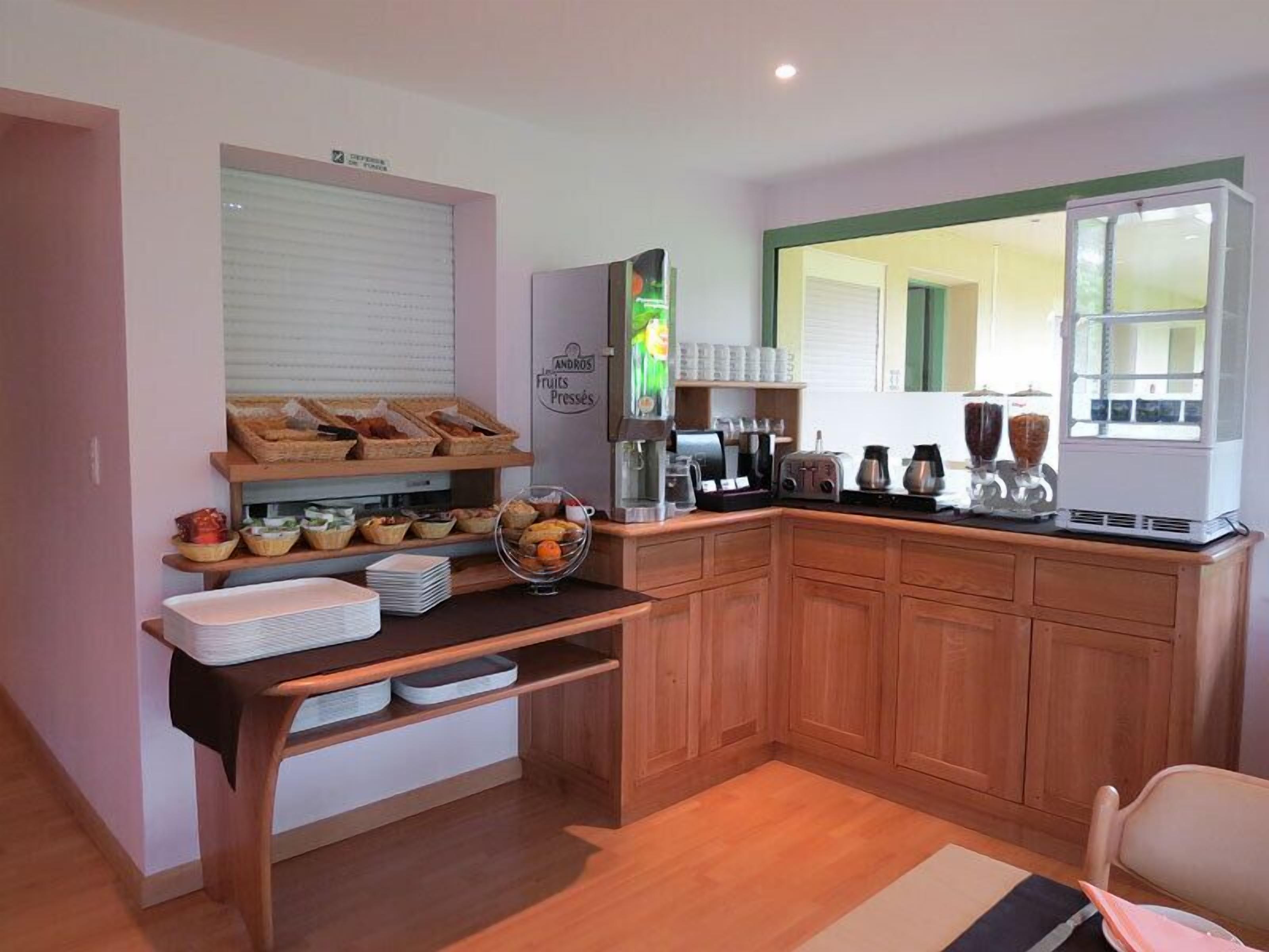 A kitchen with wooden cabinets, a breakfast bar, a coffee machine, and a fruit display.