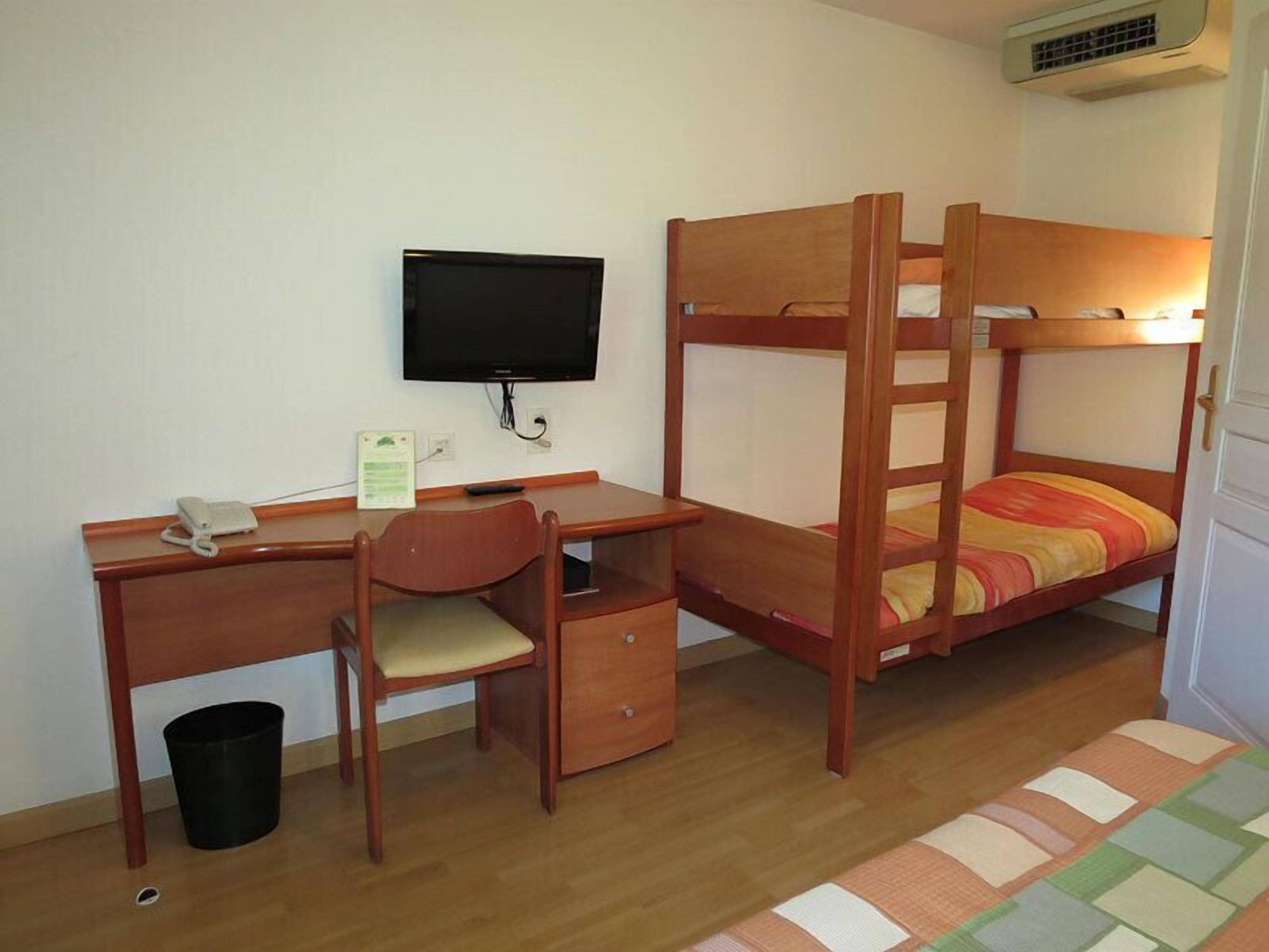 Una cama litera con escritorio y silla, un televisor y un cubo de basura.